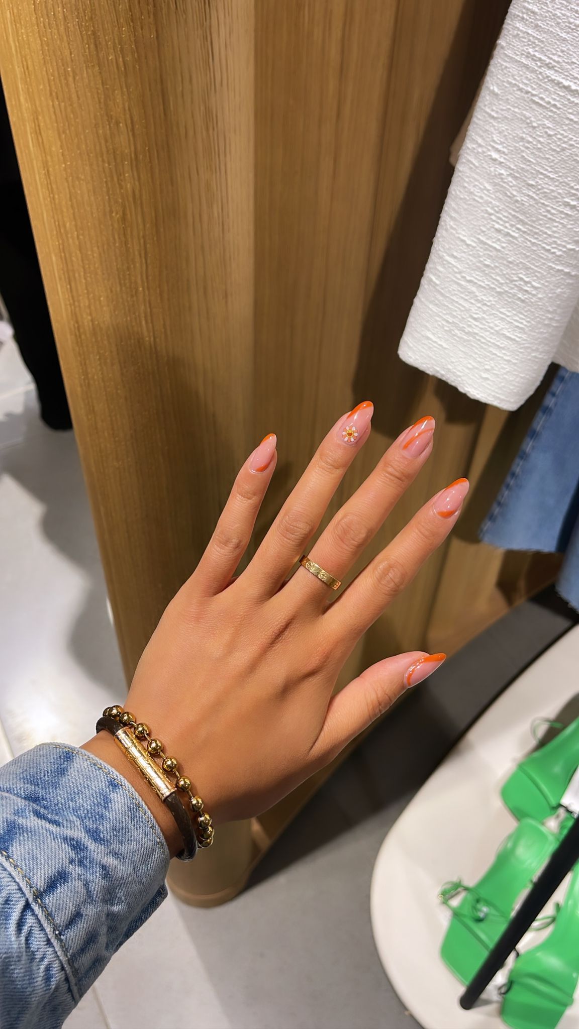 Oranje French tips met een bloemetje, hand tegen een houten paneel